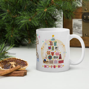 Right side view of a white glossy mug with an image design of a Christmas tree made of colorful presents, featuring a bright red image phrase "ho ho ho," with golden sparkles and a faded golden circle in the background.