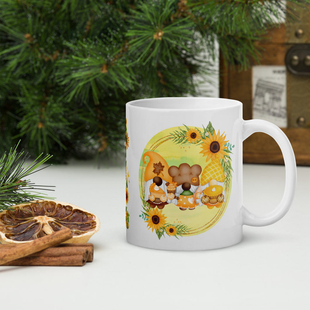 Right side view of a white glossy mug featuring a design of festive fall gnomes holding Thanksgiving desserts, encircled by a sunflower wreath on a yellowish-green background.