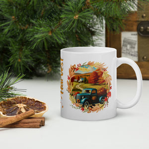 Right side view of a white glossy mug featuring a design of an old blue truck with a bed full of pumpkins on a country road, framed by a vibrant autumn leaf border, set against a late autumn day scenery.