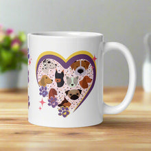 Load image into Gallery viewer, Right side view of a white glossy mug with a heart-shaped frame featuring cat ears on top, cute dog faces inside, small pink, blue, and purple paw prints on one side, and golden sparkles surrounding the frame.
