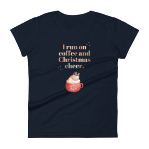 Womens fitted navy colored t-shirt with image phrase in festive font I run on coffee and Christmas cheer, with image design of festive font words, with a Christmas mug topped with whipped cream and a heart shaped topping